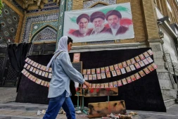 Une passante marche à côté des portraits des trois guides suprêmes de l'histoire de la République islamique d'Iran, l'ayatollah Rouhollah Khomeini, l'ayatollah Ali Khamenei et Mojtaba Khamenei (de gauche à droite), et de photos d'enfants tués lors du bombardement de l'école de Minab en février, le 25 avril 2026 à Téhéran