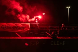 Un militant tient une fusée éclairante à côté d'une banderole "Greenpeace", lors d'une opération visant à bloquer le cargo Mikhail Dudin à Dunkerque, le 2 mars 2026 dans le Nord