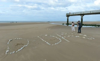 Une famille sur "Omaha Beach", où le mot "D-Day" a été tracé à l'aide de galets, à  Vierville-sur-Mer, dans le Calvados, lors des célébrations du 75e anniversaire du Débarquement en juin 2019