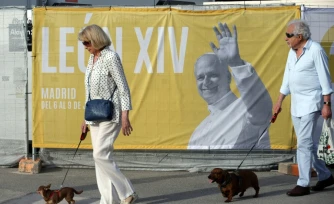 Deux personnes promènent leur chien près d'une affiche annonçant la venue du pape Léon XIV, le 5 juin 2026 à Madrid