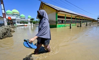 Une habitante marche près d'une mosquée dans zone inondée, le 30 novembre 2025 à Meureudu en Indonésie