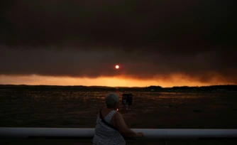 Une femme observe la fumĂ©e depuis la plage Ă Andernos-les-Bains lors d'un incendie dans la forĂȘt de LĂšge-Cap-Ferret, dans le sud-ouest de la France, le 23 juillet 2026, alors qu'une partie de la zone voisine a Ă©tĂ© Ă©vacuĂ©e