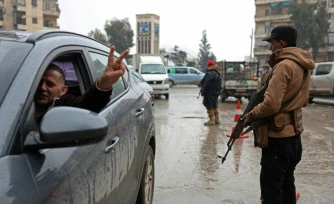 Un conducteur fait le V de la victoire en passant devant un membre des forces de syriennes, après la prise de contrôle par l'armée des quartiers kurdes d'Alep à l'issue de plusieurs jours de combats, le 11 janvier 2026