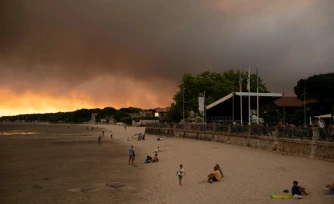 Des touristes sur la plage d'Andernos-Les Bains près de Lège Cap-Ferret où sévit un important incendie, le 23 juillet 2026 