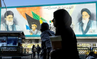 Une femme marche près d'un panneau montrant les ayatollahs Rouhollah Khomeini et Ali Khamenei, le 21 février 2026 à Téhéran