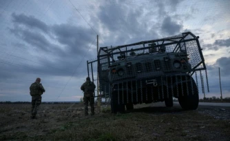 Des soldats ukrainiens devant un véhicule militaire blindé entouré d'une cage de protection contre les attaques de drones, sur une route près d'Oleksandrivka, le 6 octobre 2025