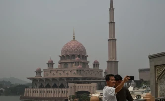 Deux personnes se prennent en photo devant une mosquée dans un air saturé par des fumées toxiques, à Putrajaya, en Malaisie, le 17 octobre 2026