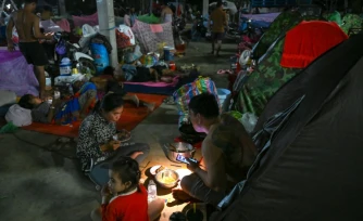 Une famille déplacée par les combats prend un repas en s'éclairant avec une lambe de poche dans un camp de la province de Banteay Meanchey, au Cambodge, le 12 décembre 2025