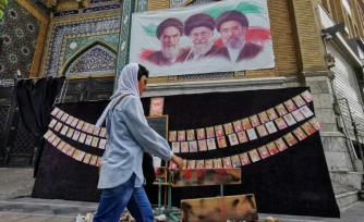 Une passante marche à côté des portraits des trois guides suprêmes de l'histoire de la République islamique d'Iran, l'ayatollah Rouhollah Khomeini, l'ayatollah Ali Khamenei et Mojtaba Khamenei (de gauche à droite), et de photos d'enfants tués lors du bombardement de l'école de Minab en février, le 25 avril 2026 à Téhéran