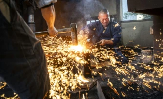 Le forgeron Akihira Kawasaki (d) maintient l'acier sur une enclume tandis que son apprenti Toru Watanabe martèle le métal pour forger des lames de katana, le 9 janvier 2026 à Misato, au Japon