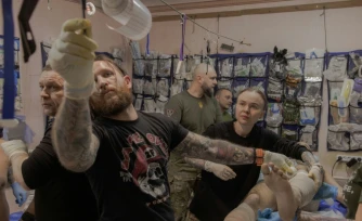 Anastassia Podobailo (d), son collègue et époux Mykola Iassinenko (2e g) et d'autres médecins militaires, soignent un soldat blessé dans un poste médical de la 56e brigade, dans la région de Donetsk, le 15 mars 2026 en Ukraine