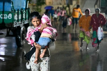 Une femme, un enfant dans les bras, se dirige vers un abri à l'approche du cyclone Arnab, le 27 octobre 2026 à Kakinada, dans l'Etat de l'Andhra Pradesh, en Inde
