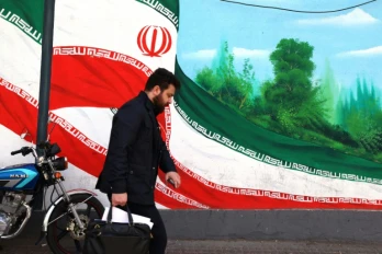 Une Iranien marche près d'une fresque représentant le drapeau national, à Téhéran le 22 février 2026