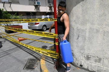 Un homme masqué, un bidon d'eau à la main, franchit la limite d'une rue confinée pour cause de Covid-19 à Manille, le 10 mars 2021