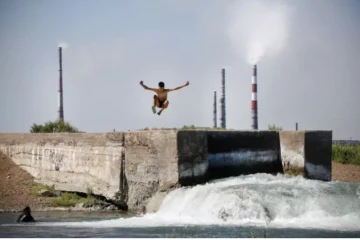 Un adolescent plonge dans de l'eau rejetée par le complexe métallurgique de Kazakhmys à Balkhach au Kazakhstan, le 20 juin 2024 ( AFP / Ruslan PRYANIKOV )