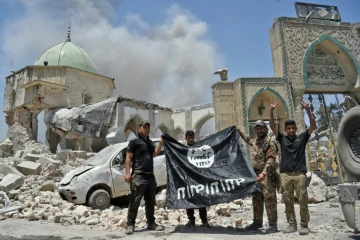 Un membre du Service du contre-terrorisme (CTS) irakien lève les bras en signe de victoire tandis que d'autres tiennent le drapeau de l'Etat islamique devant la mosquée al-Nouri de Mossoul, le 30 juin 2017