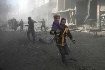 Un homme court pour sauver un enfant blessé après des bombardements du régime sur Hammouriyé, une ville du fief rebelle de la Ghouta orientale près de Damas, le 19 février 2018
