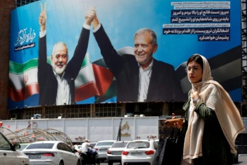 Une femme passe devant un panneau d'affichage représentant le président iranien Massoud Pezeshkian (à droite) et le chef du Hamas palestinien Ismaïl Haniyeh sur une place à Téhéran, le 8 août 2024