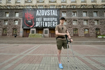 Le soldat ukrainien Vladyslav Jaïvoronok du régiment Azov, amputé d'une jambe, devant une affiche géante "Libérez les défenseurs de Marioupol", le 16 août 2022 à Kiev