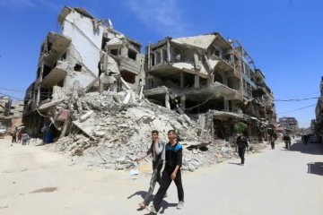Des Syriens passent devant des immeubles détruits, le 16 avril 2018 à Douma, lors d'une visite organisée par l'armée syrienne dans la Ghouta orientale