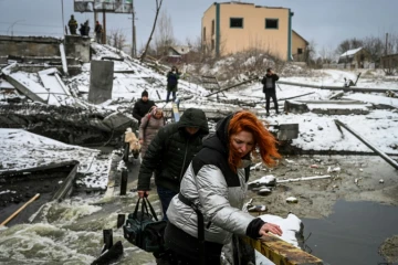 Des civils traversent une rivière sur un pont bombardé au nord de Kiev le 1er mars 2022 