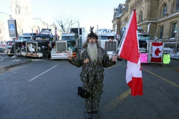 Un homme tient un drapeau du Canada près de la colline du Parlement où se trouvent des manifestants opposés aux mesures sanitaires, le 7 février 2022 à Ottawa