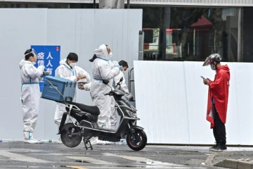 Un livreur (d) près d'employés en combinaison de protection devant un quartier confiné de Shanghai après l'apparition de nouveaux cas de Covid-19, le 17 mars 2022 en Chine