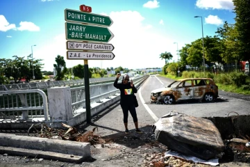 Une manifestante portant un t-shirt aux couleurs de l'UGTG (Union générale des travailleurs de Guadeloupe) lève le poing devant du matériel brûlé aux Abymes, près de Pointe-à-Pitre en Guadeloupe, le 24 novembre 2021