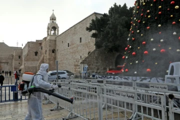 Un employé en combinaison de protection désinfecte les abords de l'église de la Nativité, avant les célébrations de Noël, le 24 décembre 2020 à Bethléem