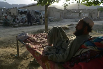 Un habitant allongé sur un lit de camp devant des maisons détruites par un séisme dans la province de Paktika, le 25 juin 2022 en Afghanistan