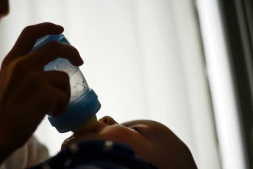 Un bébé boit son biberon dans les bras de sa mère à Paris, le 9 octobre 2012
