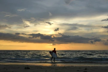 Survivant du tsunami du 26 décembre 2004, l'Indonésien Dery Setyawan porte sa planche après avoir fait du surf sur la plage de Lhoknga, le 9 décembre 2019