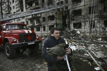 Un homme porte son chat mort devant un immeube d'habitation détruit près de Kiev, le 14 mars 2022