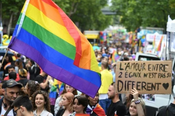 Des participants à la Marche des fiertés à Paris bradissent le drapeau arc en ciel et des pancartes, le 25 juin 2022