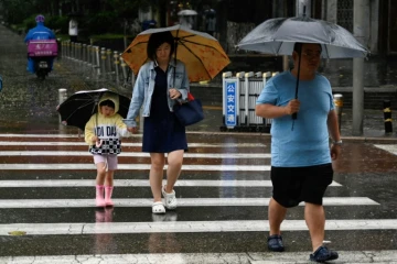 Des personnes s'abritent de la pluie avec des parapluies à Pékin, le 30 juillet 2023. La Chine a placé une partie du nord du pays en alerte rouge, y compris la région de Pékin, en raison de pluies torrentielles attendues suite à l'avancée du typhon Doksuri.