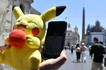 Un joueur tient une mascotte de Pokémon et joue au Pokémon Go sur son portable, le 19 juillet 2016 à Rome. 