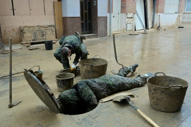 Des soldats évacuent la boue d'un égout à Paiporta, au sud de Valence, dans l'est de l'Espagne, le 13 novembre 2024, à la suite d'inondations meurtrières