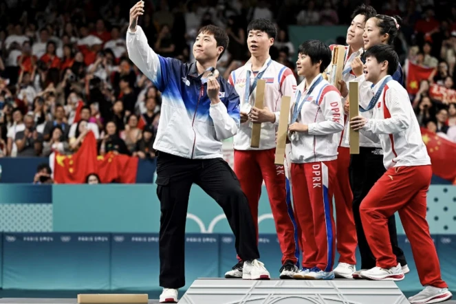 Le pongiste sud-coréen Lim Jonghoon (à gauche) célèbre sa médaille de bronze avec les nord-coréens Ri Jong Sik et Kim Kum Yong, les athlètes chinois Wang Chuqin et Sun Yingsha, ainsi qu'avec sa compatriote Shin Yubin à l'issue de l'épreuve du double mixte aux Jeux olympiques de Paris 2024, le 30 juillet 2024. (JUNG YEON-JE / AFP)