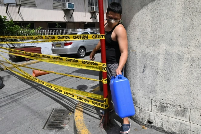 Un homme masqué, un bidon d'eau à la main, franchit la limite d'une rue confinée pour cause de Covid-19 à Manille, le 10 mars 2021