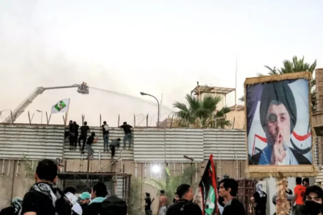 Des soutien du leader religieux chiite Moqtada Sadr, dont l'effigie s'affiche sur un panneau (d), essaient d'escalader la barrière devant l'ambassade de Suède à Bagdad, le 20 juillet 2023 ( AFP / Ahmad AL-RUBAYE )