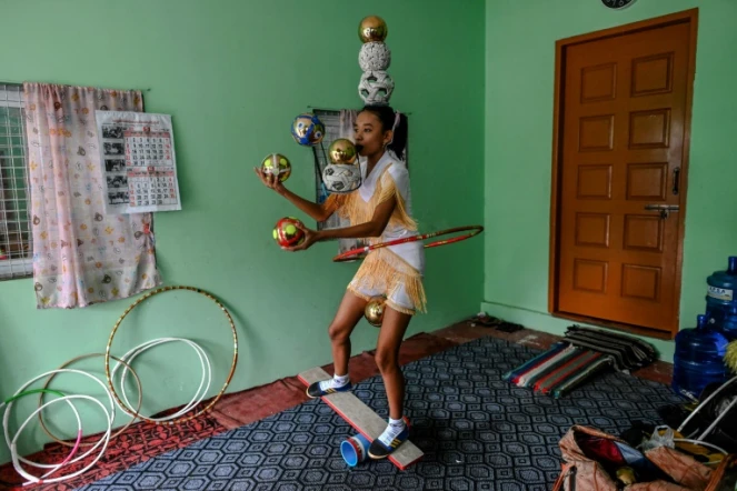 Han Myint Mo tient en équilibre une balle dorée sur la lame d'un couteau, le manche entre ses dents, lors d'un entraînement de jonglage, le 5 juillet 2022 à Rangoun, en Birmanie