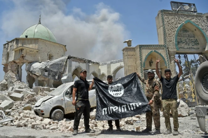 Un membre du Service du contre-terrorisme (CTS) irakien lève les bras en signe de victoire tandis que d'autres tiennent le drapeau de l'Etat islamique devant la mosquée al-Nouri de Mossoul, le 30 juin 2017