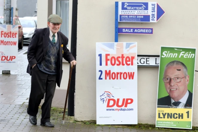 Un homme près d'une affiche du Sinn Féin, partisan d'une réunification de l'Irlande, et d'une affiche du Parti démocratique unioniste DUP, favorable à l'union avec la Grande-Bretagne, le 2 mars 2017 près de Brookeborough