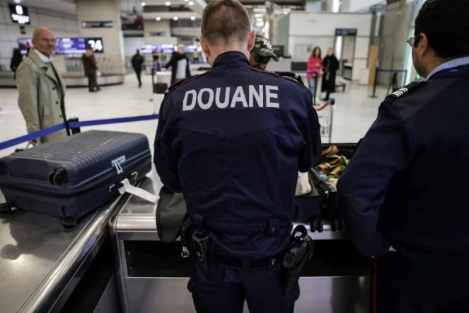 Des douaniers inspectent les bagages de passagers à l'aéroport de Roissy-Charles-de-Gaulle, au nord de Paris, le 21 mars 2025 