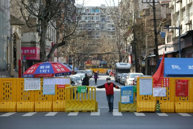 Un homme devant une barrière empêchant l'enrée dans un quartier confiné de Wuhan, le 15 mars 2020 pendant l'épidémie du nouveau coronavirus