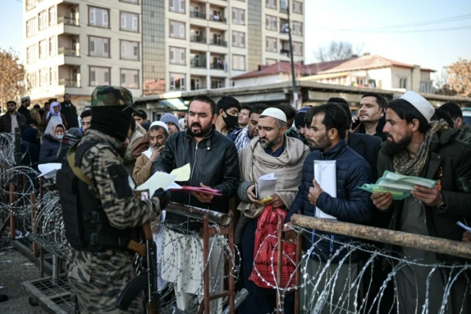 Un combattant taliban inspecte les documents de personnes faisant la queue devant le bureau des passeports à Kaboul, le 18 décembre 2021