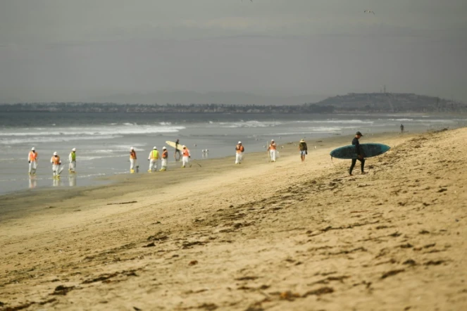 Un surfeur regagne la plage de Huntington Beach, en Californie, tandis que des équipes de nettoyage s'affairent à nettoyer l'impact de la marée noire, le 4 octobre 2021