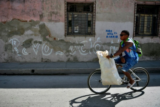 Un homme passe en vélo devant un graffiti "Revolucion" à Santiago de Cuba, le 31 décembre 2018