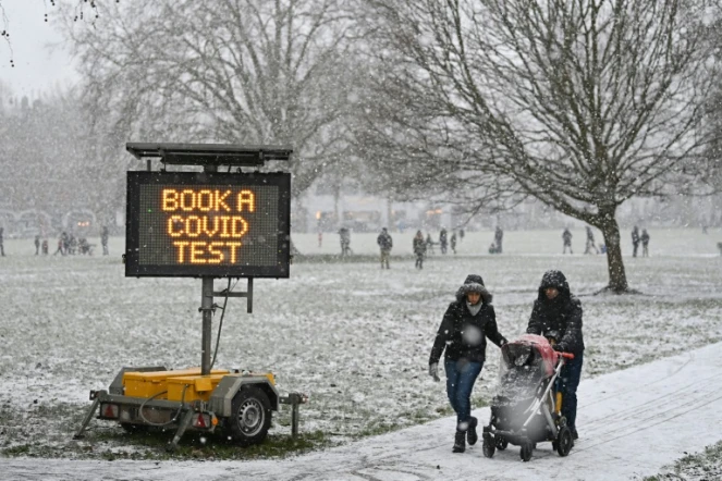 Des promeneurs passent près d'un panneau appelant à se faire tester au Covid-19, dans un parc de Londres sous la neige, le 24 janvier 2021