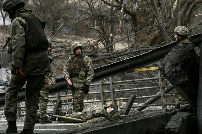 Des militaires ukrainiens se préparent à transporter le corps d'un camarade sur une civière dans la ville d'Irpin, au nord-ouest de Kiev, le 13 mars 2022